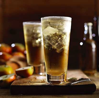 Sparkling cider in a glass with ice, sliced apple in the background