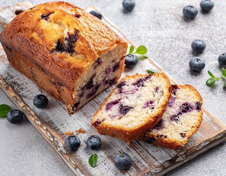 Blueberry pound cake on a wooden board, surrounded by scattered blueberries