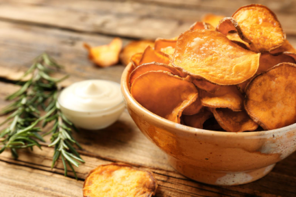Bowl of crispy sweet potato chips on a rustic wooden table with fresh rosemary and a creamy dipping sauce