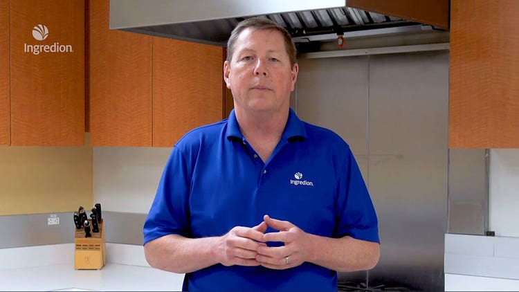 Man in blue shirt presenting in a kitchen, discussing savory product formulations.