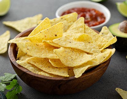 Close-up of tortilla chips with avocado in background, representing snack ingredient solutions