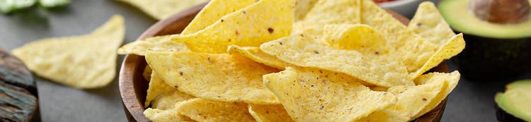 Bowl of tortilla chips with avocado in background, representing snack ingredient solutions
